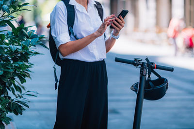 Midsection of woman using phone while standing with scooter on road