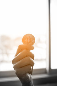 Close-up of hand holding ice cream cone against window