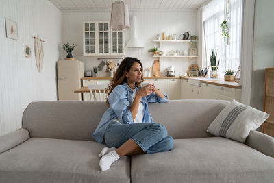 Young woman using phone while sitting on sofa at home