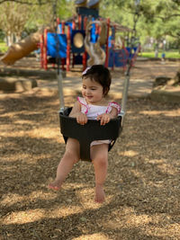 Full length of cute girl sitting on swing