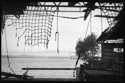 Rope hanging on pole by sea against sky