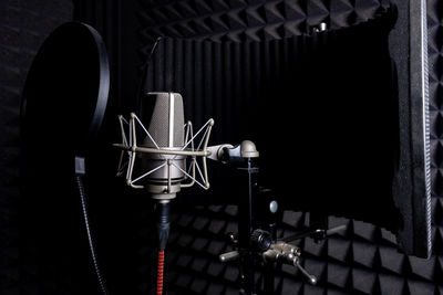 Contemporary metal microphone with wire placed on background of soundproof foam with pyramid shaped pattern in dark music recording studio