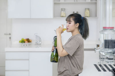 Side view of young woman drinking alcohol in kitchen at home