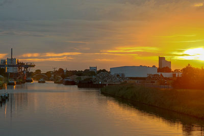 Buildings by river against sky during sunset