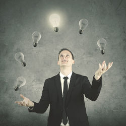 Digital composite image of businessman juggling light bulbs against wall