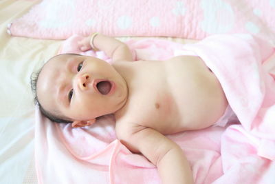 High angle portrait of baby yawning while lying on bed