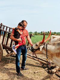 Man with daughter standing by bull on field