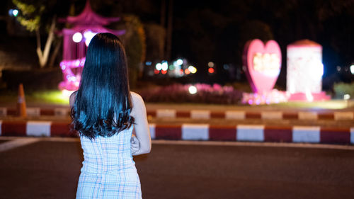 Rear view of woman standing against illuminated city at night