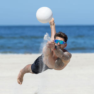 Shirtless man playing volleyball at beach