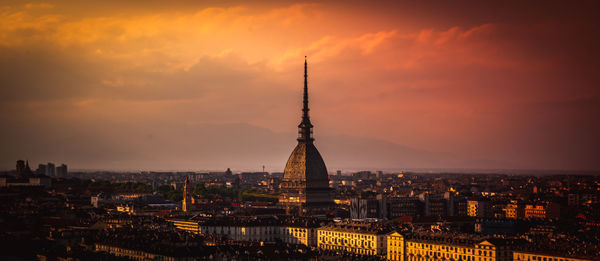 Illuminated buildings in city against sky during sunset