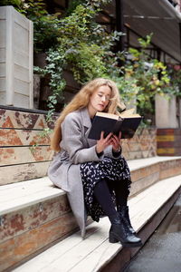 Young woman reading book while sitting on steps