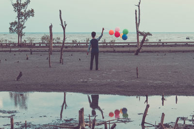 Boy playing with balloons at beach against sky