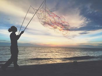 Silhouette man fishing on beach against sky during sunset