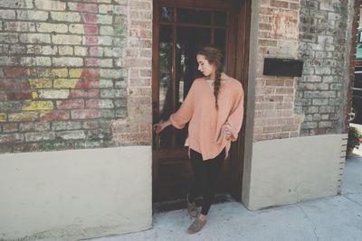 Young woman holding doorknob while standing at doorway