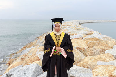 Young woman wearing graduation gown on groyne at sea