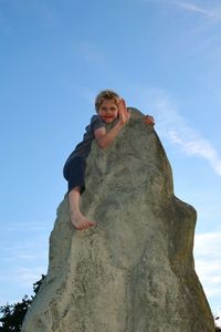 Low angle portrait of boy on rock against sky