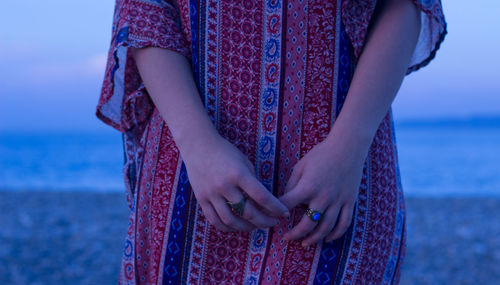 Midsection of woman standing at beach during sunset