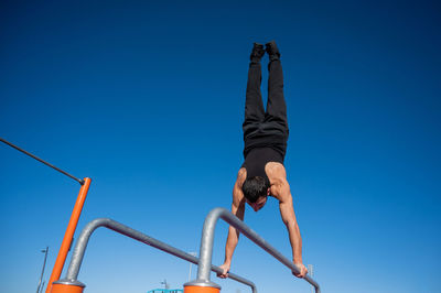Low angle view of man climbing on rope against clear blue sky