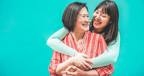 Smiling daughter embracing mother against turquoise background