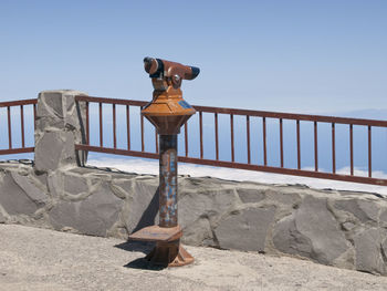 Railing by sea against clear blue sky