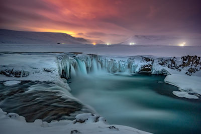 Scenic view godafoss falls on snowcapped mountains against sky during sunset