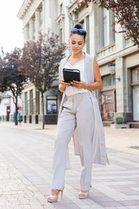 Portrait of young woman standing on footpath in city