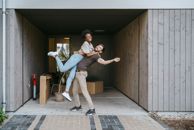 Happy man picking up girlfriend while standing at building entrance