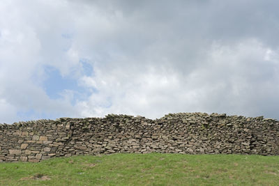 Low angle view of stone wall on field against sky