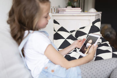 Side view of cute girl using digital tablet sitting at home