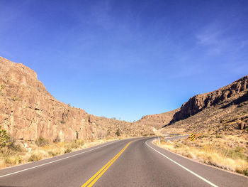 Empty road along rocky mountains against sky