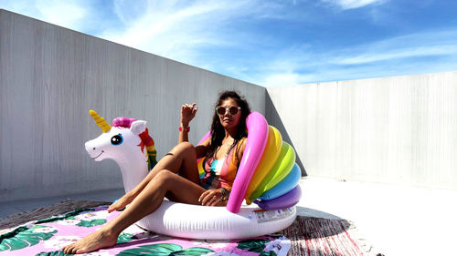 Young woman sitting like poolside against sky with unicorn for fun