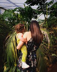 Mother carrying daughter standing by tree