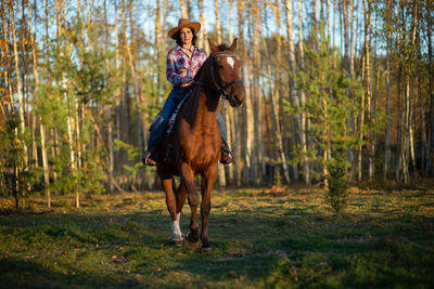 A woman wearing a cowboy hat rides a horse in a countryside farm yard,natural soft sunlight