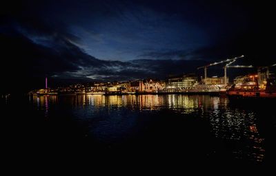 Illuminated city by river against sky at night