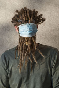 Woman wearing mask with dreadlocks against wall