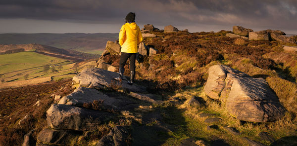 Rear view of woman standing on rock against sky