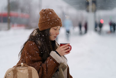 Asian woman on railway platform trying to keep warm while waiting for train delayed by snowfall