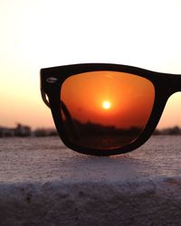 Close-up of sunglasses against sky during sunset