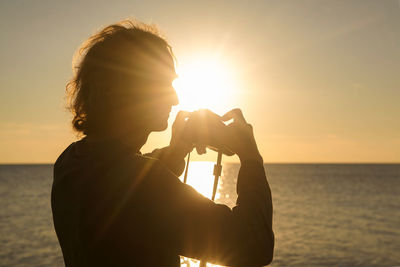 Silhouette man photographing sea against clear sky during sunset