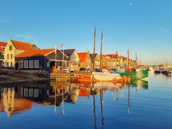 Sailboats moored on harbor by buildings against blue sky