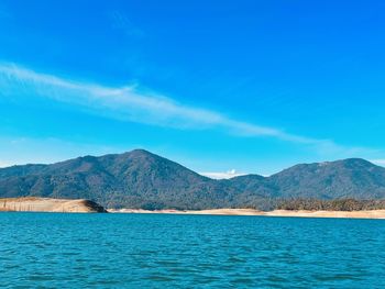 Scenic view of sea and mountains against blue sky