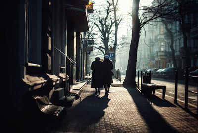 Rear view of people walking on sidewalk in city