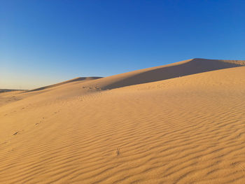 Sand dunes in desert against clear blue sky