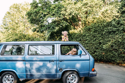 Two girls sitting on and in vintage blue van in summertime