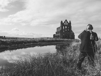 Rear view of woman standing on grassy field with whitby abbey in background