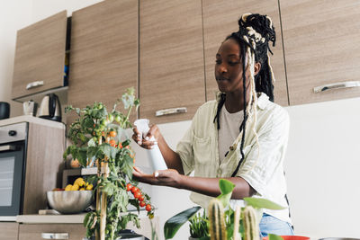 Young woman watering house plant at home