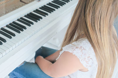 High angle view of blond woman sitting by grand piano at home