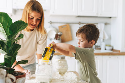 Young woman mother and her toddler boy son have fun while cooking with flour at table in kitchen 