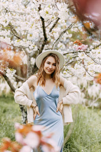 Gentle girl in a dress and a fashionable hat is walking enjoying the smell of blooming flowers