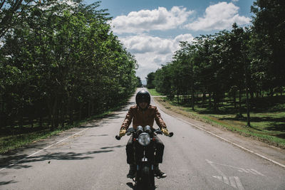 Man riding bicycle on road against trees